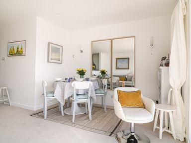 A dining area with a round table set for four and a white swivel chair with a yellow pillow at Sea Point in Exmouth