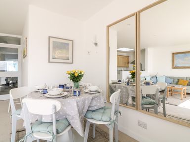 A dining area with a round table set for four with bowls and cups a vase with yellow flowers and white chairs with blue cushions at Sea Point in Exmouth