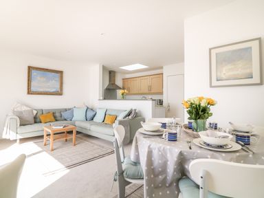 A living room with a sectional sofa and a dining table set with dishes and flowers at Sea Point in Exmouth