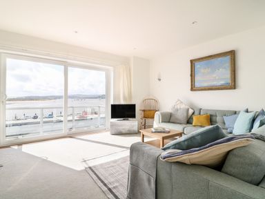 A living room with a gray sectional sofa a wooden chair a small wooden coffee table a flat screen TV and a large sliding glass door overlooking water at Sea Point in Exmouth