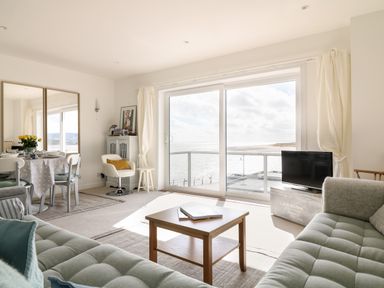 A living room with two gray sofas a wooden coffee table a dining table with chairs and large sliding glass doors overlooking the sea at Sea Point in Exmouth