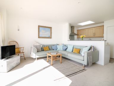 A living room with a sectional sofa pillows a wooden chair a small table a television and a kitchen counter with wooden cabinets at Sea Point in Exmouth