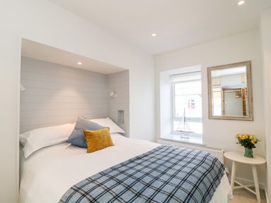 A bedroom with a bed with pillows a window with a model sailboat a mirror and a side table with flowers at Sea Point in Exmouth