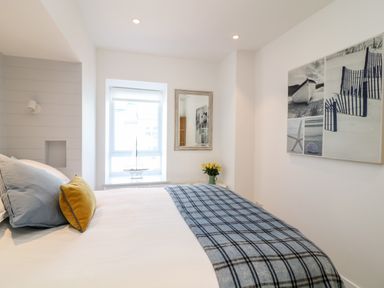 A bedroom with a bed covered in white and blue plaid blanket with pillows a window with a model sailboat a wall mirror and a wall art with sea-themed images at Sea Point in Exmouth