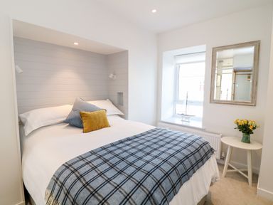 A bedroom with a bed with white bedding and two pillows a window a small white round table with yellow flowers and a wall mirror at Sea Point in Exmouth