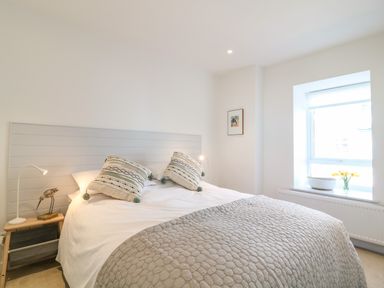 A bedroom with a bed white bedding patterned cushions bedside table with lamp and bird decor window with flowers and basket at Sea Point in Exmouth