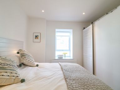 A bedroom with a bed with patterned pillows a window with flowers and a basket and a sliding door closet at Sea Point in Exmouth