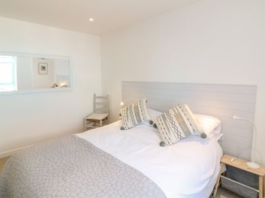 A bedroom with a bed with two patterned pillows a gray quilt a small wooden chair and a nightstand with a lamp at Sea Point in Exmouth