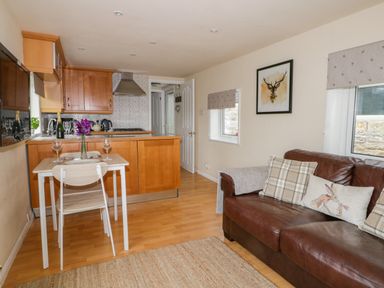 A kitchen and living area with wooden cabinets a dining table with two chairs and a brown leather sofa at Thirley Beck Lodge in Harwood Dale