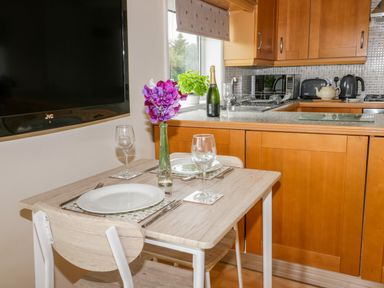 A kitchen with wooden cabinets dining table set with plates glasses and a vase with flowers at Thirley Beck Lodge in Harwood Dale