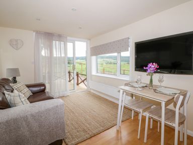 A living room with a leather sofa a small dining table with two chairs and a wall-mounted TV at Thirley Beck Lodge in Harwood Dale