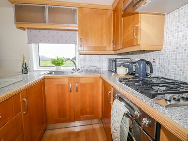 A kitchen with wooden cabinets a gas stove a kettle a teapot a sink and a window at Thirley Beck Lodge in Harwood Dale