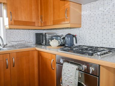 A kitchen corner with wooden cabinets a gas stove an oven a kettle a teapot a toaster and a microwave at Thirley Beck Lodge Harwood Dale