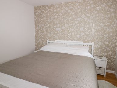 A bedroom with a bed covered with beige blanket and a white nightstand at Thirley Beck Lodge in Harwood Dale