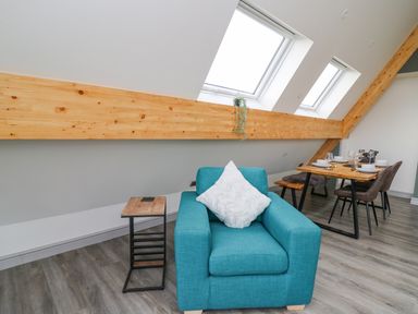 A room with a turquoise armchair and a side table near skylight windows and a dining table with chairs at Elan Valley Welsh - The Sheepfold in Llanyre near Llandrindod Wells