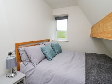 A bedroom with a bed pillows a lamp on a bedside table and a window at Elan Valley Welsh - The Sheepfold in Llanyre near Llandrindod Wells