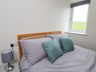 A bedroom with a bed with gray bedding and two teal pillows next to a window at Elan Valley Welsh - The Sheepfold in Llanyre near Llandrindod Wells