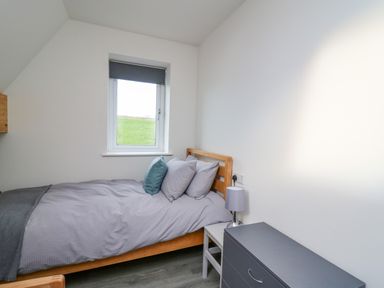 A bedroom with a wooden bed a window gray bedding a small side table with a lamp and a gray dresser at Elan Valley Welsh - The Sheepfold in Llanyre near Llandrindod Wells