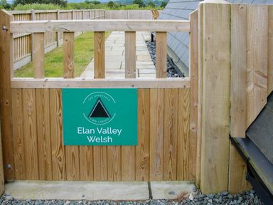 A wooden gate with a green sign saying Elan Valley Welsh at The Sheepfold in Llanyre near Llandrindod Wells