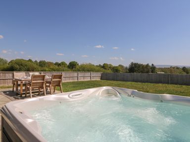 An outdoor space with a hot tub and a wooden table with chairs on a patio at Elan Valley Welsh - The Sheepfold Llanyre near Llandrindod Wells