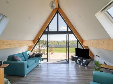 A living room with teal sofas a television and large triangular windows opening to a garden at Elan Valley Welsh - The Sheepfold in Llanyre near Llandrindod Wells