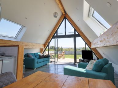 A living room with two blue sofas a television and large triangular windows opening to an outdoor patio at Elan Valley Welsh - The Sheepfold in Llanyre near Llandrindod Wells