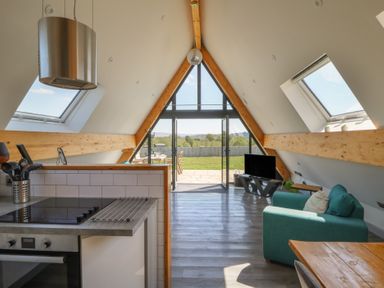 An open plan living area with a kitchen, green sofa, TV, dining table, and large windows at Elan Valley Welsh - The Sheepfold in Llanyre near Llandrindod Wells