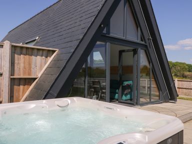 An outdoor hot tub next to a modern A-frame cabin with glass doors and a view of a patio at Elan Valley Welsh - The Sheepfold Llanyre near Llandrindod Wells