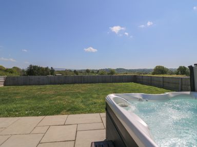A garden with grass a fence and a hot tub on a paved patio at Elan Valley Welsh - The Sheepfold in Llanyre near Llandrindod Wells
