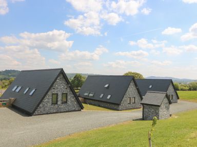 Three stone and slate buildings with pitched roofs on a gravel driveway in a rural area at Elan Valley Welsh - The Sheepfold in Llanyre near Llandrindod Wells