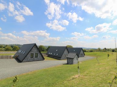 Three stone buildings with black roofs on a gravel driveway surrounded by grass and trees at Elan Valley Welsh - The Sheepfold in Llanyre near Llandrindod Wells