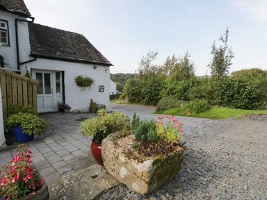An outdoor area with potted plants and a stone planter outside a white building at Rusland View Rusland near Newby Bridge