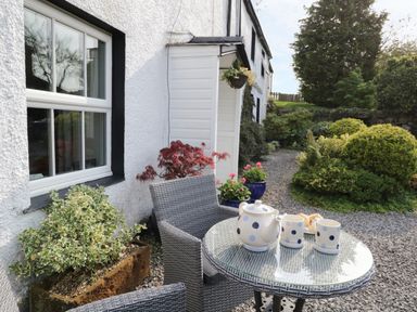 An outdoor patio area with a round glass table and two chairs beside a white house with plants around at Rusland View Rusland near Newby Bridge