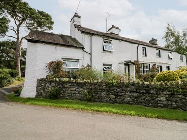 A white stone cottage with multiple windows and a stone wall in front at Rusland View Rusland near Newby Bridge
