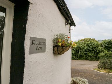 A white wall with a sign reading Rusland View and a hanging basket with flowers and greenery outside Rusland View Rusland near Newby Bridge