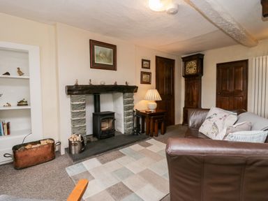 A living room with a fireplace a brown leather sofa and a grandfather clock at Rusland View Rusland near Newby Bridge