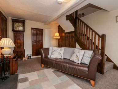 A living room with a leather sofa and patterned cushions near wooden stairs and a grandfather clock at Rusland View Rusland near Newby Bridge