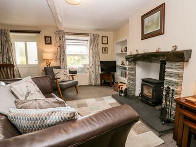 A living room with a brown leather sofa a gray armchair a wood burning stove and a television at Rusland View Rusland near Newby Bridge