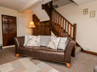 A living room with a brown leather sofa under wooden stairs and a floor lamp at Rusland View Rusland near Newby Bridge