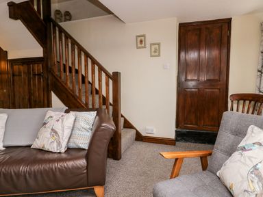 A living room with a brown leather sofa and gray chair near wooden stairs and a closed wooden door at Rusland View Rusland near Newby Bridge