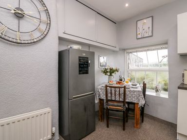 A kitchen corner with a dining table set for breakfast next to a window and a refrigerator under wall cabinets at Rusland View Rusland near Newby Bridge