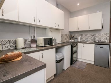A kitchen with white cabinets a microwave a kettle a stove a dishwasher and a loaf of bread on the counter at Rusland View Rusland near Newby Bridge