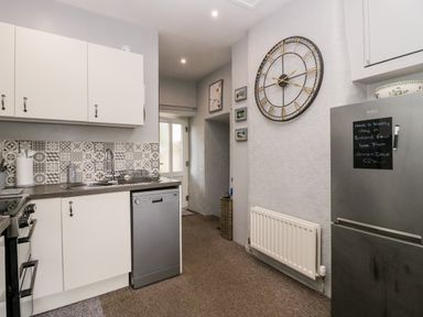 A kitchen with white cabinets stainless steel dishwasher large wall clock and a refrigerator with a message at Rusland View Rusland near Newby Bridge