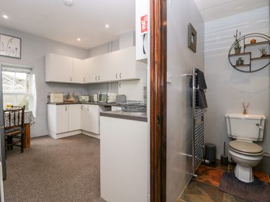 A kitchen with white cabinets and appliances next to a bathroom with a toilet and towel rack at Rusland View Rusland near Newby Bridge