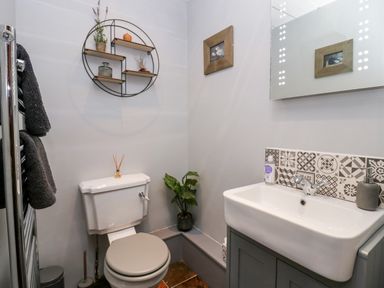 A bathroom with a toilet, sink with patterned tiles, wall shelves with decor, towels, and a small plant at Rusland View Rusland near Newby Bridge