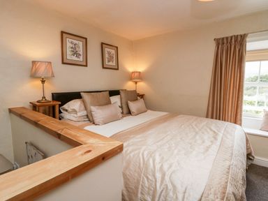 A bedroom with a bed with beige bedding two framed floral pictures on the wall and a window with curtains at Rusland View Rusland near Newby Bridge