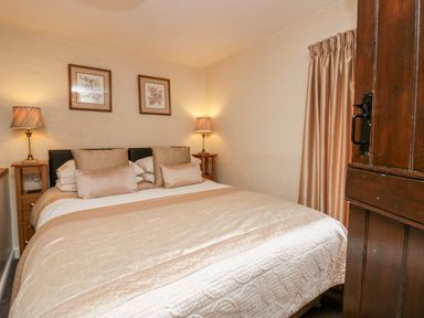 A bedroom with a bed with beige bedspread two bedside tables with lamps two framed pictures on the wall and curtains at Rusland View Rusland near Newby Bridge