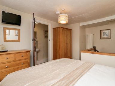 A bedroom with a bed a wooden dresser a wardrobe a television and an open door showing a bathroom at Rusland View Rusland near Newby Bridge