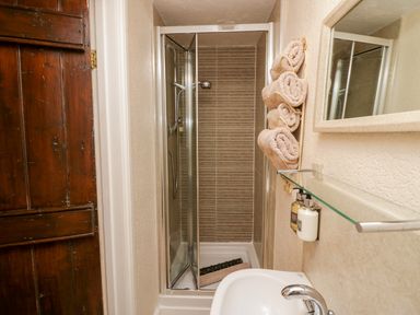 A small bathroom with a shower cubicle rolled towels on the wall and a sink at Rusland View Rusland near Newby Bridge