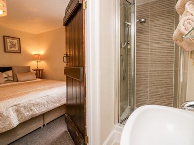 A bedroom with a bed lamp and framed picture next to a bathroom with a shower and sink at Rusland View Rusland near Newby Bridge